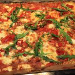 Pizza med tomater, ost och ruccola på en plåt, gräddad till gyllenbrun färg.