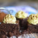 Fyrkantiga bitar av chokladkaka med grädde och kakao på toppen, placerade på en träyta.