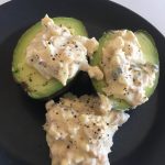 Halverad avokado fylld med äggsallad och svartpeppar på en svart tallrik.