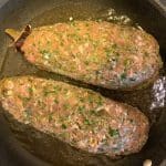 Två köttfärslimpor med örter som ligger i en stekpanna med vätska.