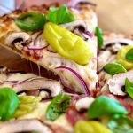 En skiva pizza med svamp, lök, basilika och gröna paprikor på toppen.