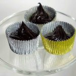 Tre chokladpraliner i silver- och guldfärgade aluminiumformar på en glasskiva.