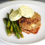 Köttfärsbiff serverad med sparris och skivor av örtsmör på en vit tallrik.