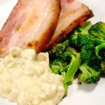 Två skivor grillad bacon med broccoli och en krämig sås på en vit tallrik.