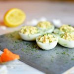 Fyra halvor av fyllda ägg med dill på en svart skärbräda, med citron i bakgrunden.