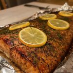 Grillad laxfilé med citronskivor och örter på en aluminiumfolie.