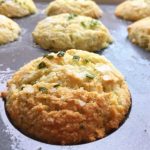 Bakade muffins med gräslök i en muffinsplåt, med gyllene yta och gröna bitar av gräslök.