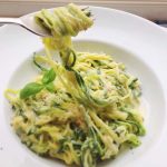 En portion pasta med zucchini och en krämig sås, garnerad med färsk basilika.