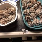 En skål med chokladbollar täckta av kokosflingor, placerade på en svart yta.