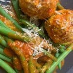 Köttbullar serverade med gröna bönor och tomatsås, toppade med riven ost.