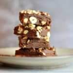 En stapel av chokladfudge med hackade nötter på en tallrik.