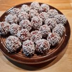 En tallrik med chokladbollar rullade i kokosflingor, placerade på en brun tallrik.
