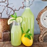 Grön dryck i en glasflaska och ett mindre glas, med citron och mynta som dekoration.