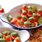 Caprese-spett med körsbärstomater, mozzarella och basilika på tandpetare i en skål.