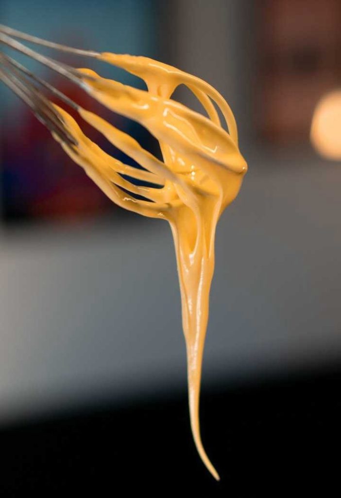 Crème Toum - Libanesisk vitlökssås 6 En visp med gul sås som droppar ner från spetsen i en suddig bakgrund.