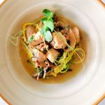 En tallrik med kyckling, grönsaker och sås, serverad med nudlar.