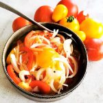 En skål med tomatsallad bestående av skivade tomater och lök, med hela tomater i bakgrunden.