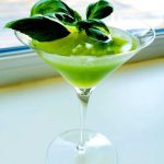 Grön cocktail i ett martiniglas med basilika som garnering.