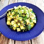 En tallrik med zucchini och äppelbitar blandat med örter och frön på en blå tallrik.