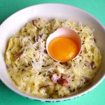 Skål med pasta, bacon, riven ost och ett rått ägg i mitten.
