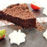 En bit chokladkaka med riven choklad på toppen, omgiven av jordgubbar och grädde.