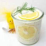 Glass jar filled with lemon cream topped with lemon slices and dill, next to a yellow decorative chick.