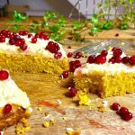 En kaka med kokosfrosting och röda vinbär på toppen, delvis skuren på en träyta.