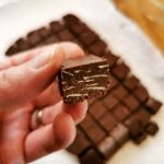 En hand som håller en bit chokladfudge med flera bitar i bakgrunden.