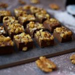 En plåt med chokladfudge toppad med hackade valnötter, placerad på en yta med strössel av socker.
